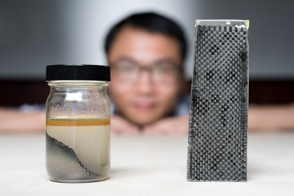 Kai Yu, a former postdoctoral researcher in The George W. Woodruff School of Mechanical Engineering at Georgia Tec, sits behind a piece of carbon fiber composite immersed in alcohol. (Credit: Rob Felt, Georgia Tech)